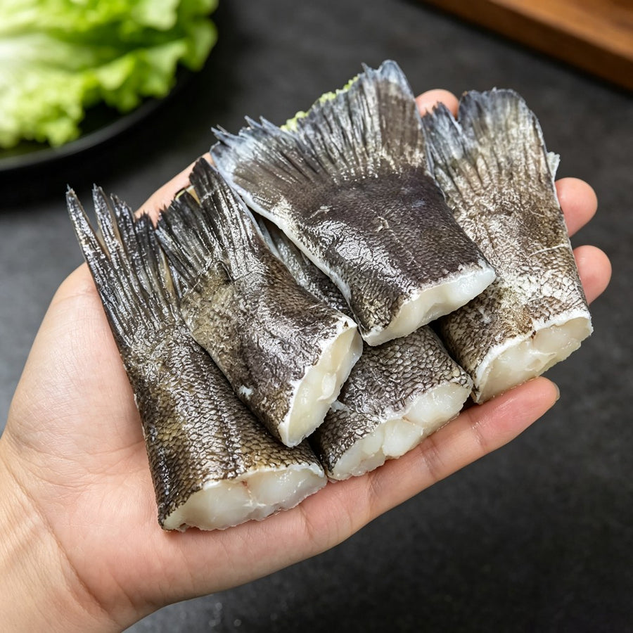Hand holding several skin-on cod tails above a dark surface