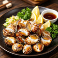 Spotted sea snails piled on a dark plate with lemon wedges